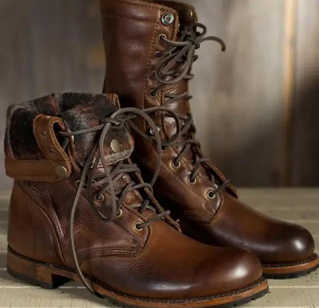 A pair of brown leather lace-up boots, one with the shaft folded down to reveal a fur lining, on a wooden surface.