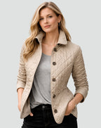 Front view of a woman wearing a tan diamond quilted jacket over a grey t-shirt, with plaid-lined cuffs rolled.