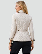 Back view of a woman wearing a cream diamond quilted jacket, showing the tailored waist and plaid-lined cuffs.