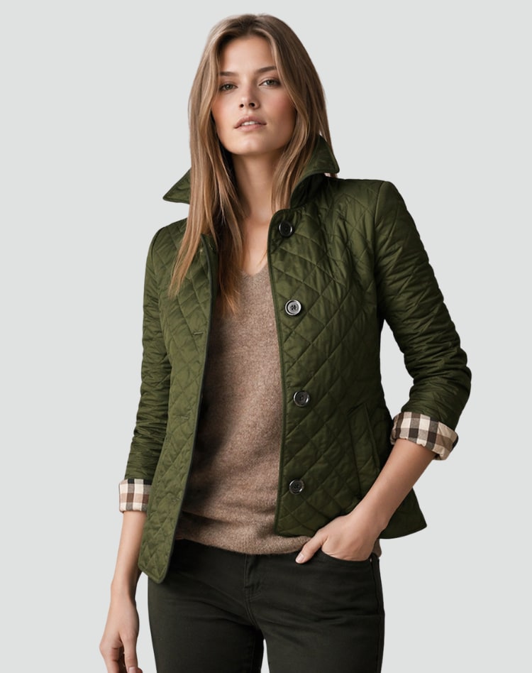 A woman models a green quilted jacket with cuffed sleeves revealing a plaid lining, paired with a brown sweater and dark green pants.